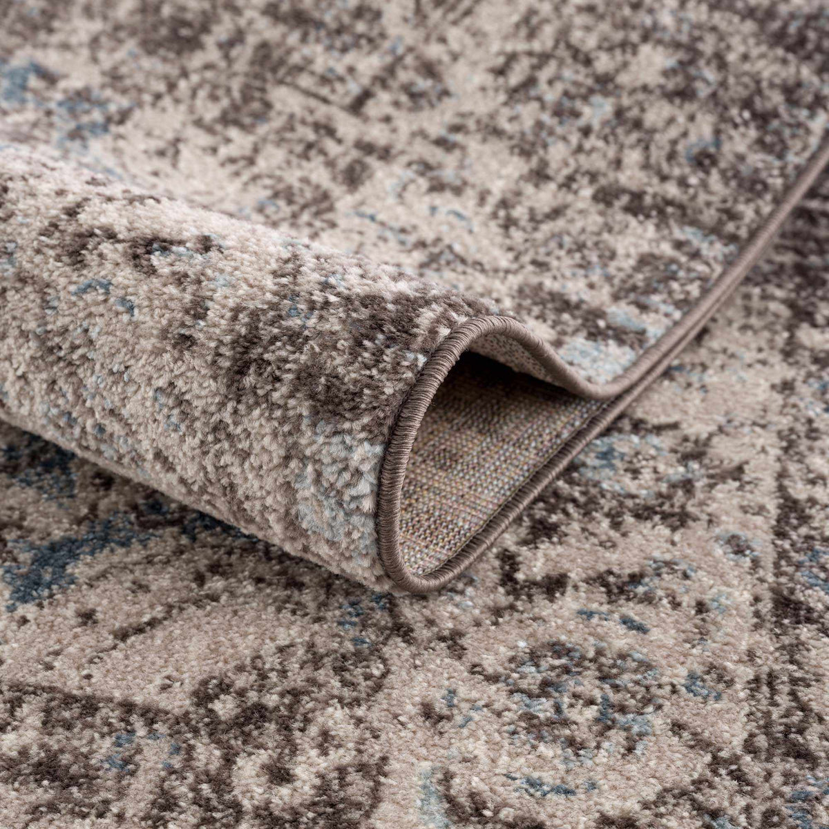 Dark brown medallion area rug by Hauteloom with intricate pattern, shown folded on a neutral background.