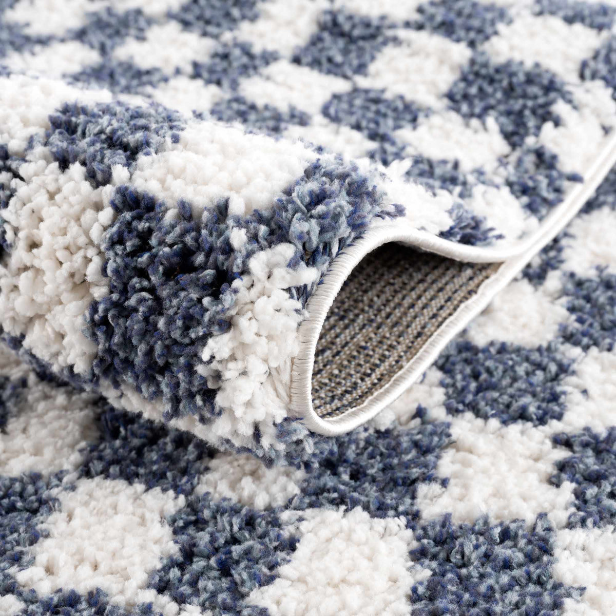Blue and white checkered area rug from Boutique Rugs, showcasing the patterned fabric and folded corners on a neutral surface.