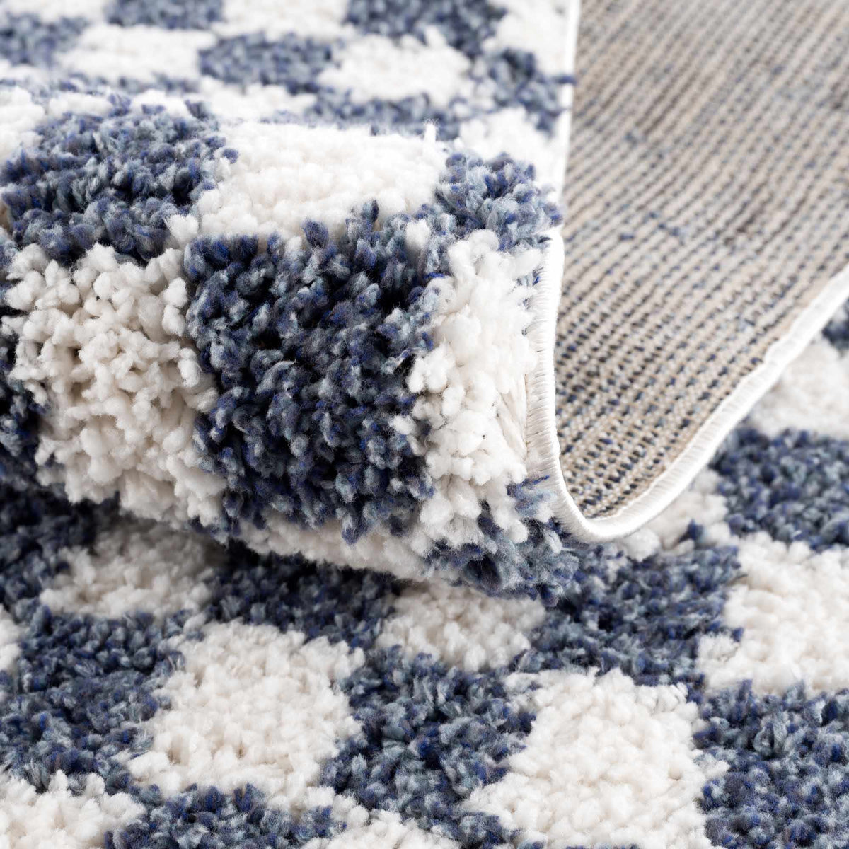 Blue and white checkered area rug from Boutique Rugs, showing a folded section with a classic checkered pattern and textured fabric.