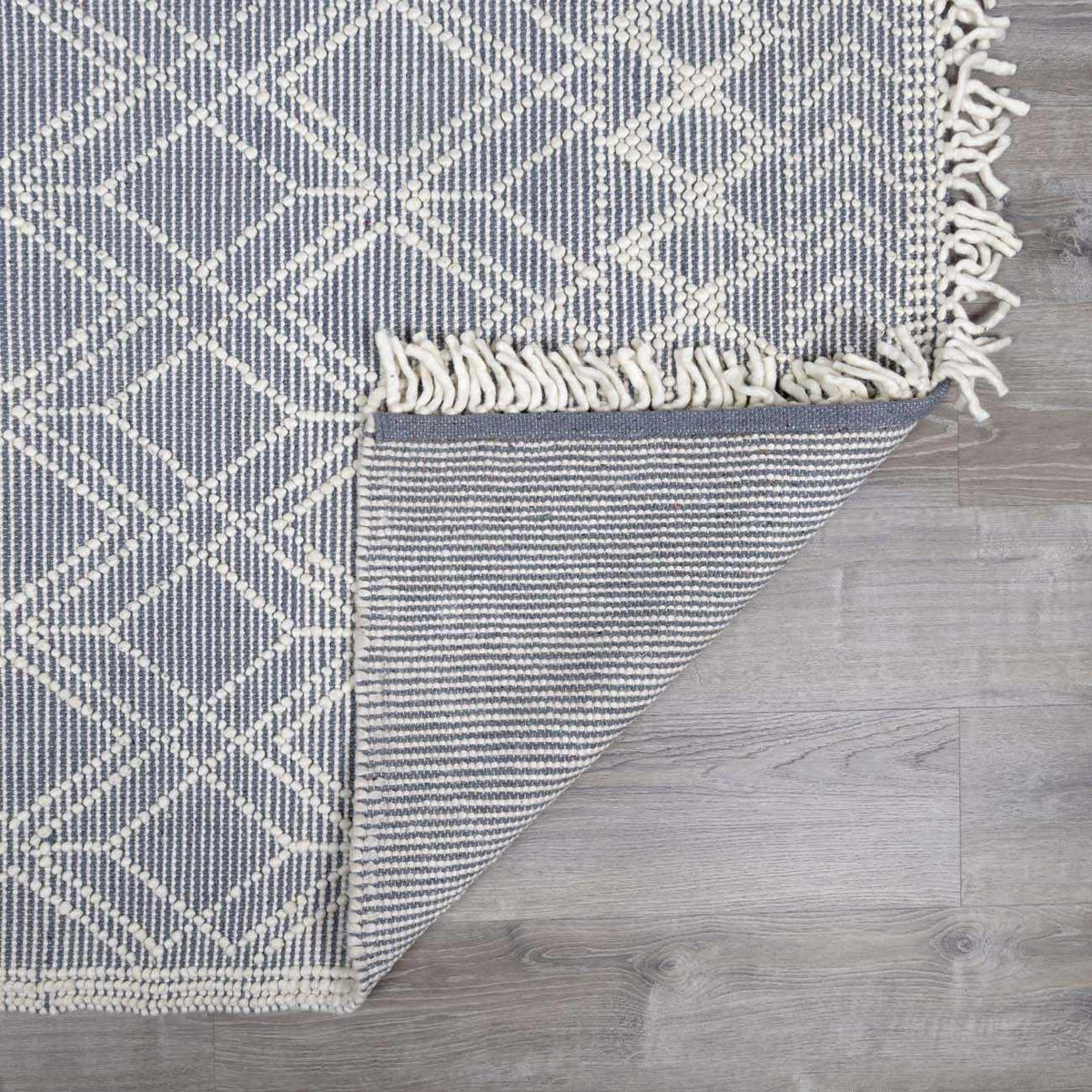 Boutique Rugs Ramsbury Denim Blue Wool Rug folded, textured wool surface, soft blue tones, cozy and stylish home decor.