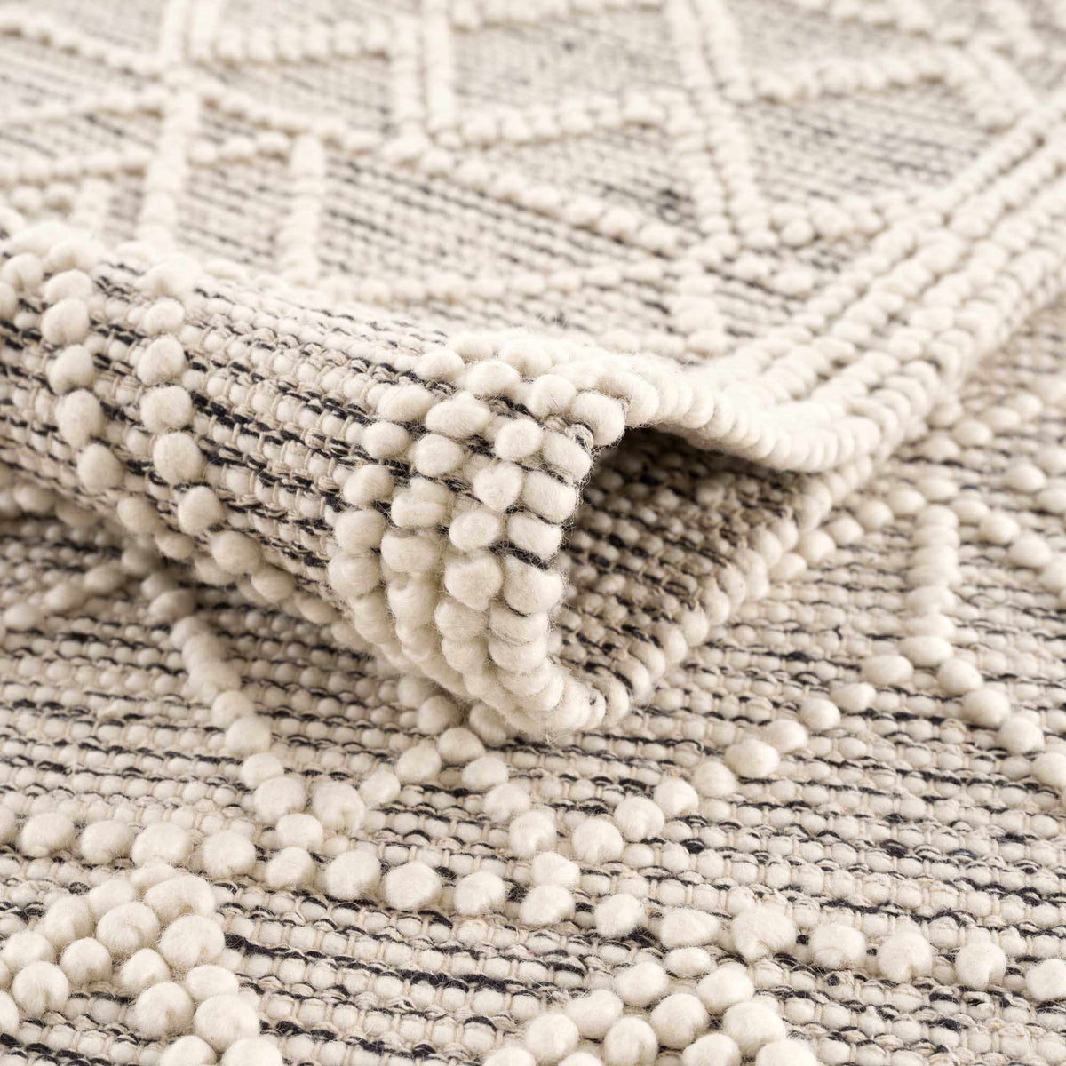 Hauteloom Ramsbury area rug with geometric patterns in neutral tones, displayed folded on a studio background.