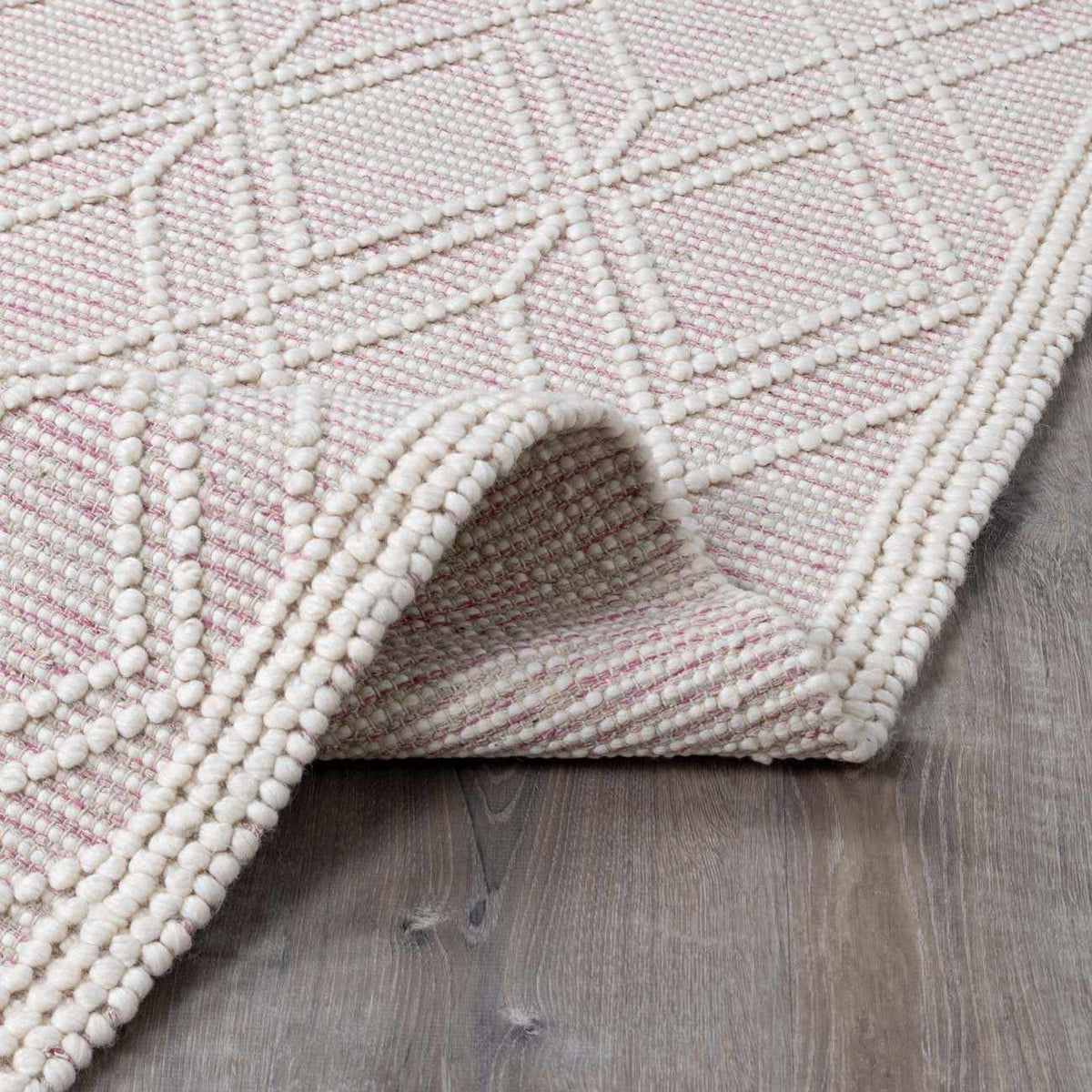 Soft pink wool rug by Boutique Rugs, folded to show plush texture and elegant design, ideal for cozy living spaces.