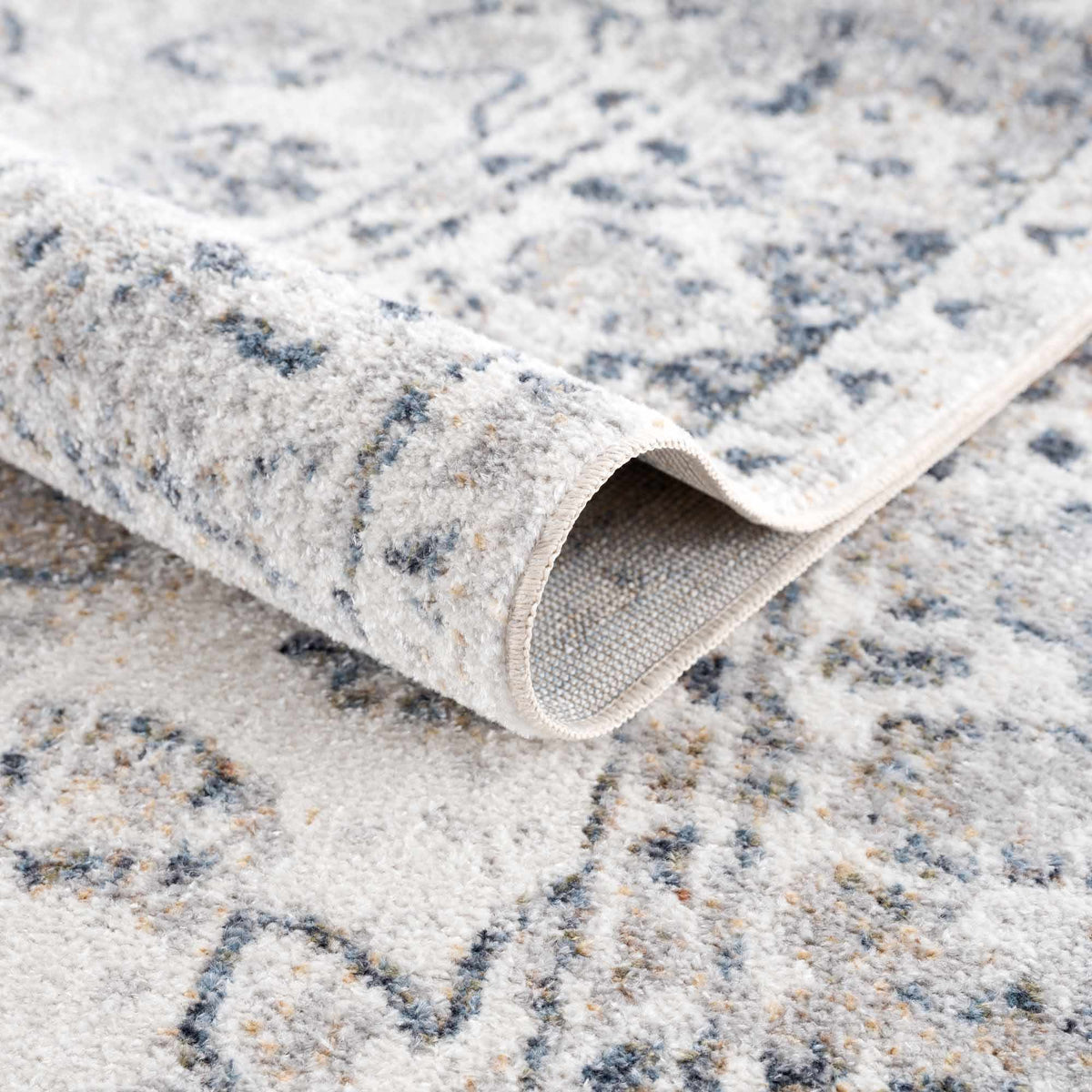 Folded beige Rudo Flat Pile Washable Rug by Boutique Rugs, showcasing soft texture and durable design in a cozy indoor setting.