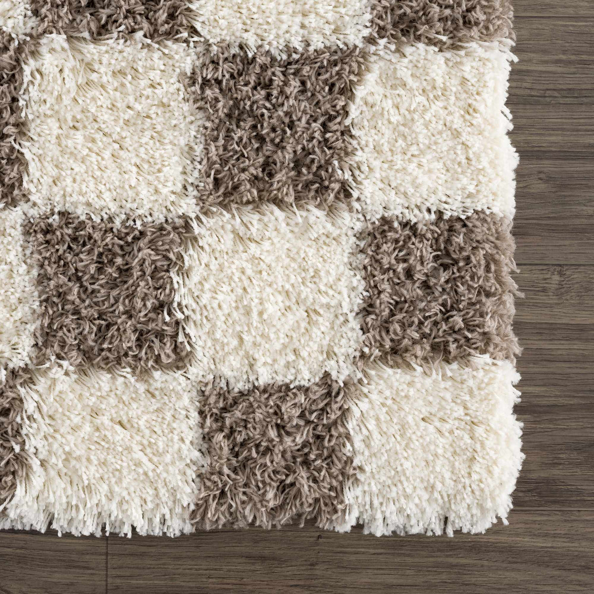 Corner view of Boutique Rugs Atira Brown Checkered Area Rug with a brown and beige checkered pattern on a wooden floor.