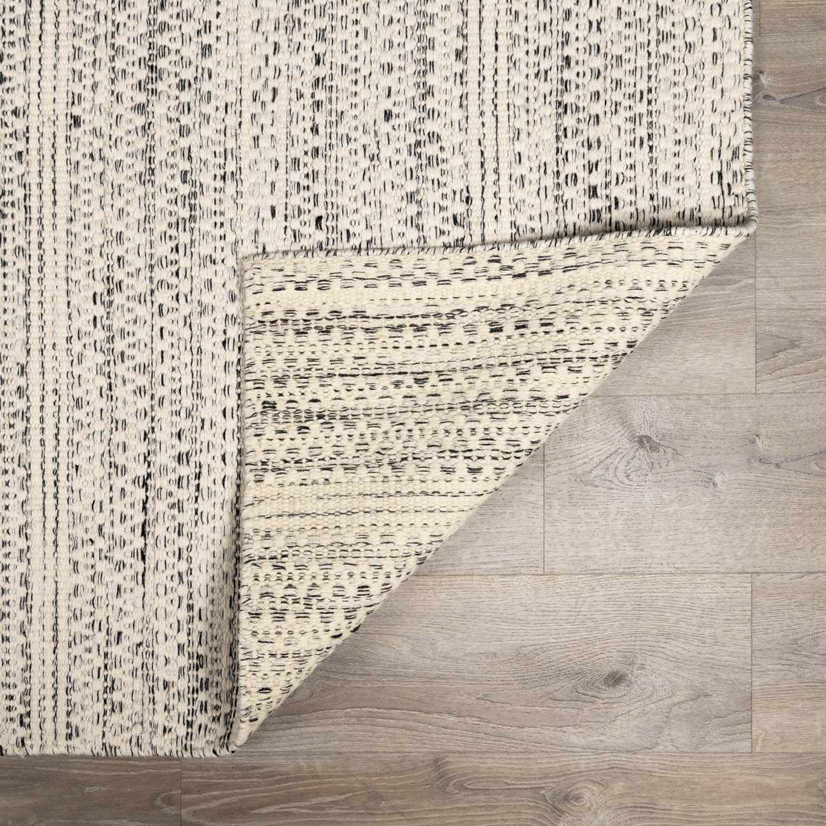 Hauteloom Williford Wool Area Rug with intricate geometric pattern in neutral tones, shown folded on a wooden floor.